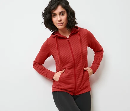 Femme posant en veste à capuche rouge et leggings noirs.