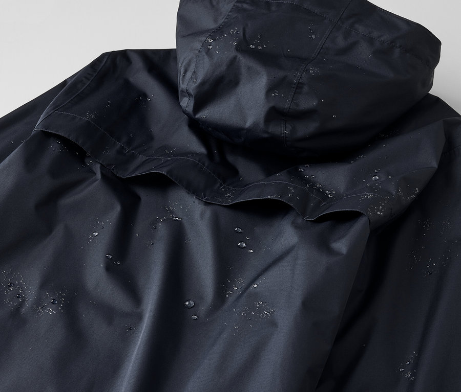 Vue détaillée d'une veste de pluie unisexe avec une capuche, sur laquelle se trouvent des gouttes d'eau.