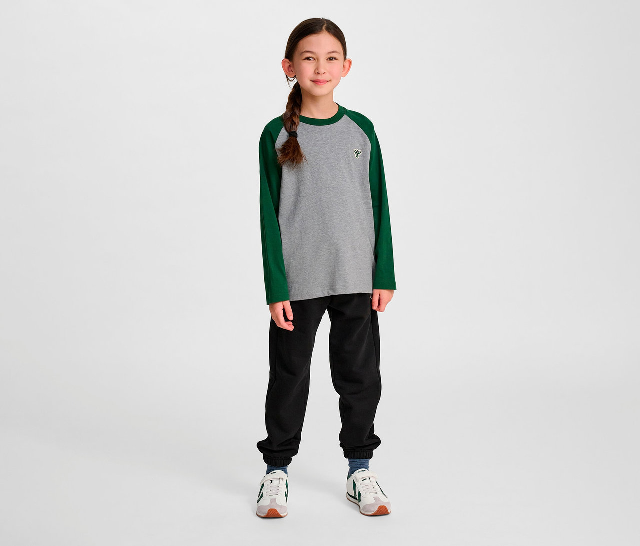 Une fille debout porte un t-shirt ample à manches raglan vert HUMMEL HMLJR BEE.