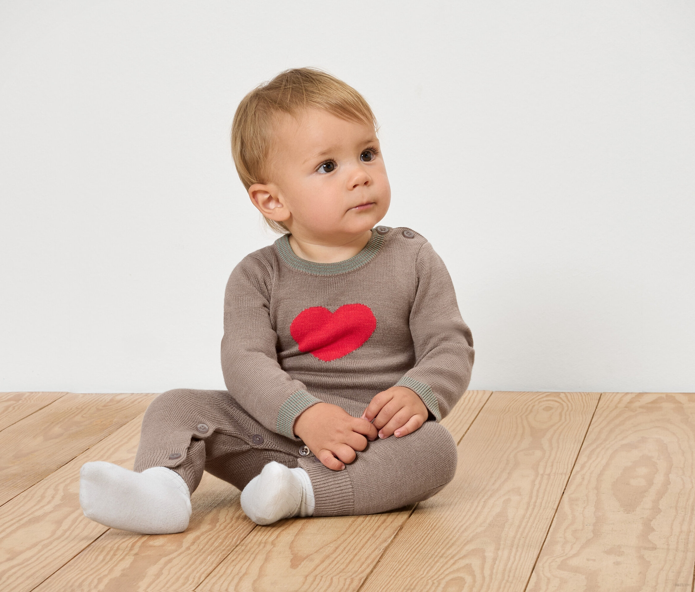 Un bébé est assis sur un plancher en bois et porte des vêtements bruns avec un cœur.