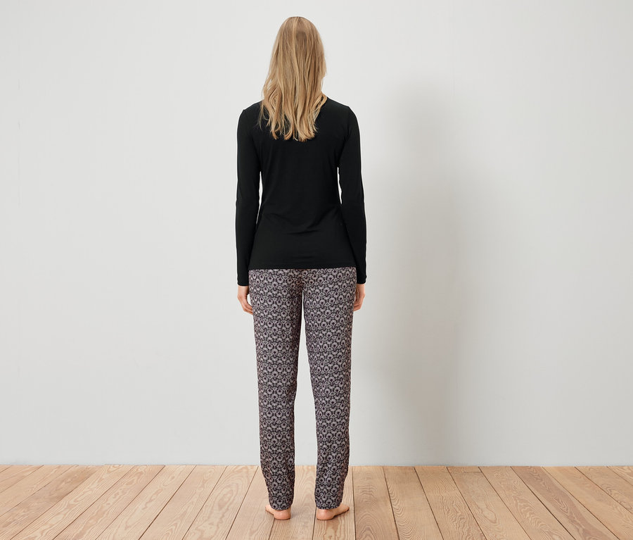 Une femme, vue de dos, porte un T-shirt noir à manches longues et un pantalon à motifs.