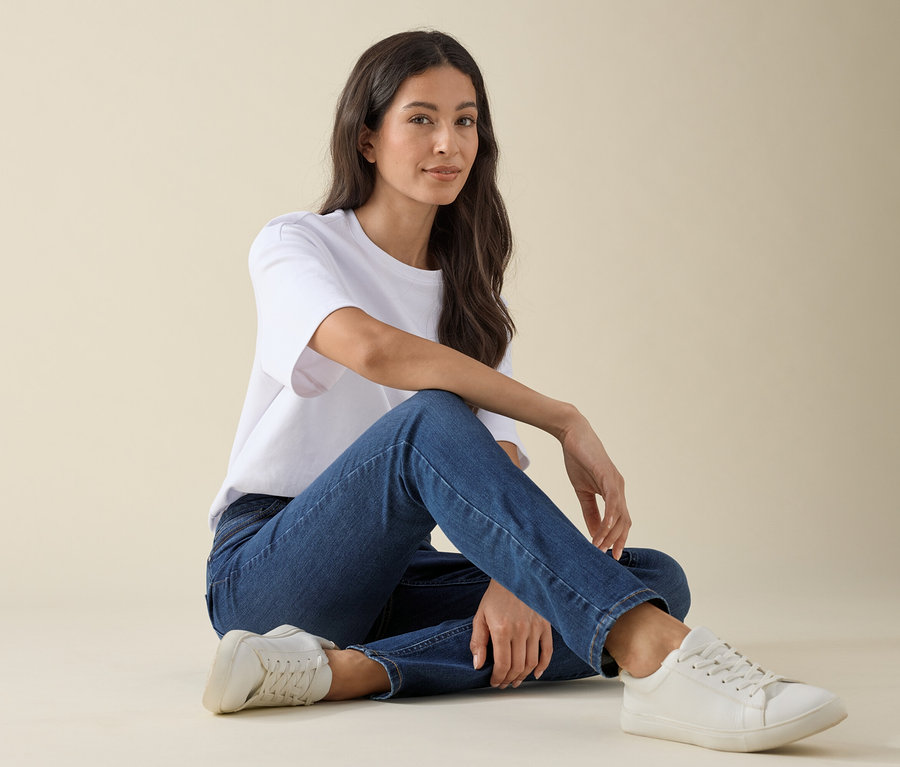Femme assise par terre portant un jean slim – Coupe « Emma », denim bleu moyen, un t-shirt blanc et des baskets.