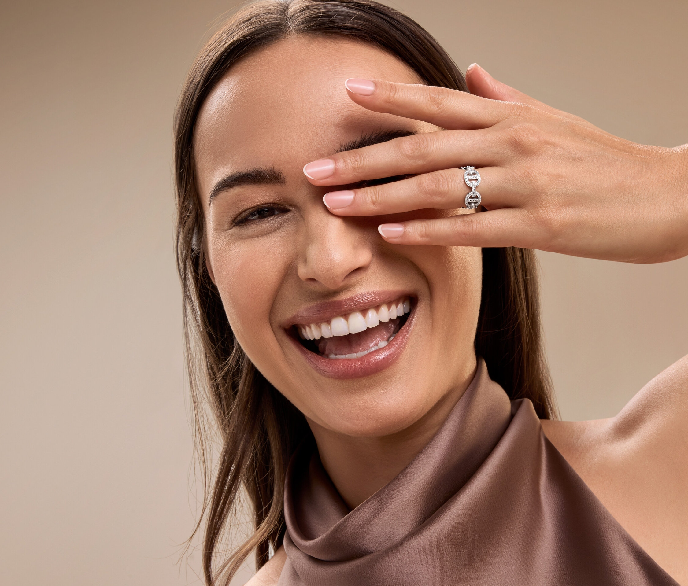Une femme souriante se couvre l'œil avec sa main, elle porte une bague argentée à l'annulaire.