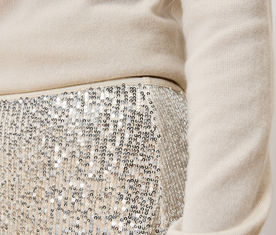Détail d'une tenue féminine : pull crème et jupe à paillettes argentées.