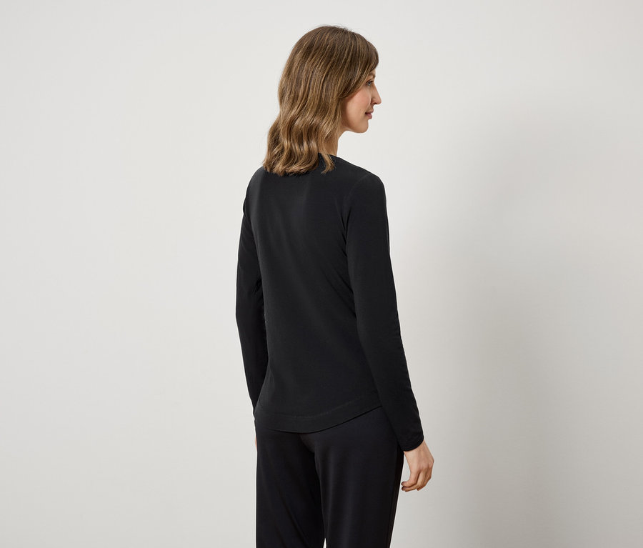 Une femme vue de dos porte un t-shirt noir à manches longues et un pantalon noir.