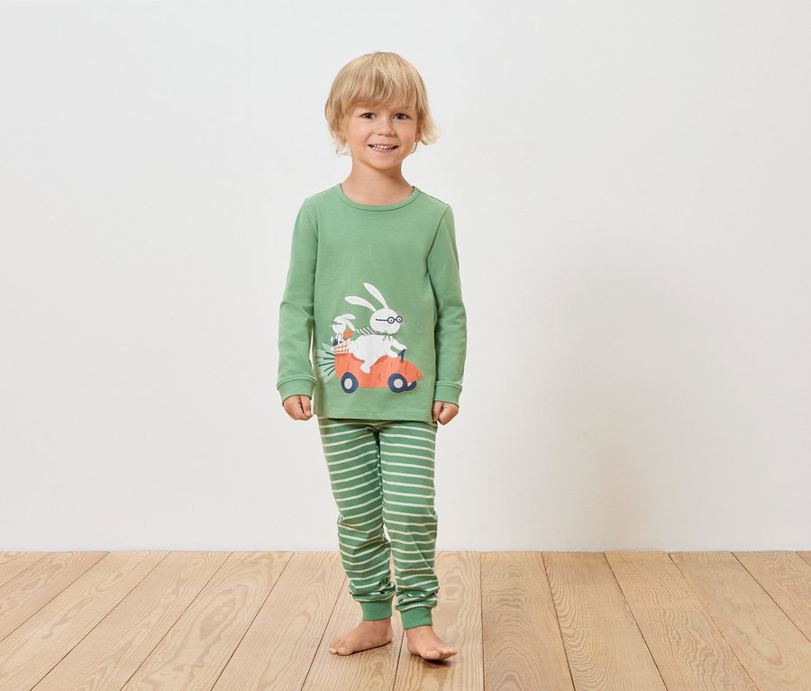 Un garçon porte un pyjama vert à manches longues et un pantalon rayé avec un motif de lapin dans une voiture.