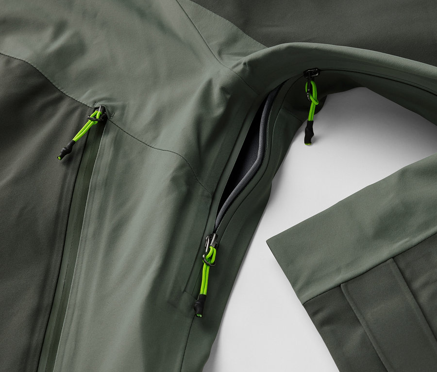 Gros plan sur une veste outdoor 3 couches avec une poche ouverte et des détails de fermeture éclair vert néon.