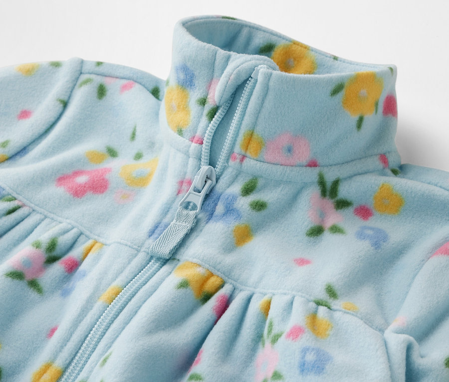 Gros plan sur une veste polaire pour enfant avec fermeture éclair et motif floral.
