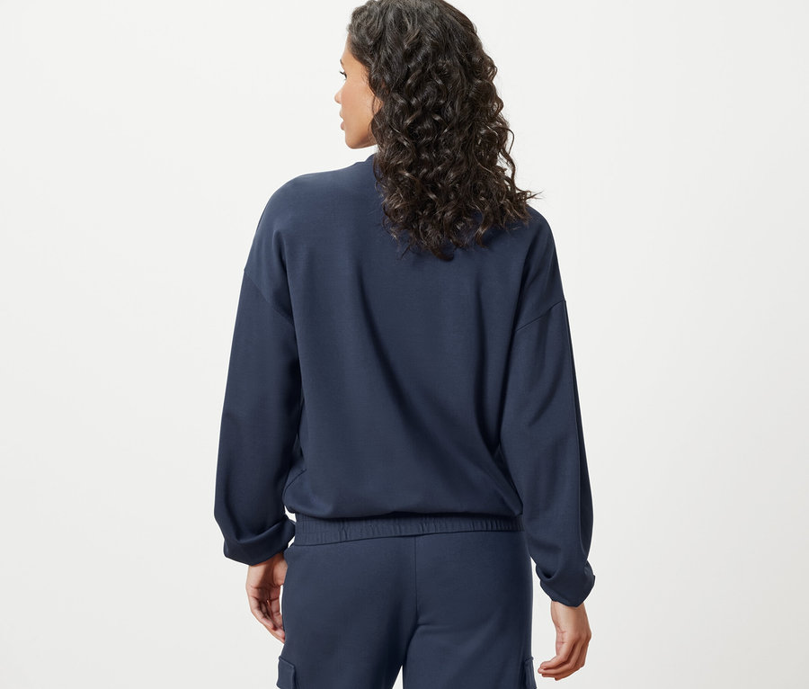Vue arrière d'une femme aux cheveux ondulés foncés portant une veste de survêtement bleu marine.