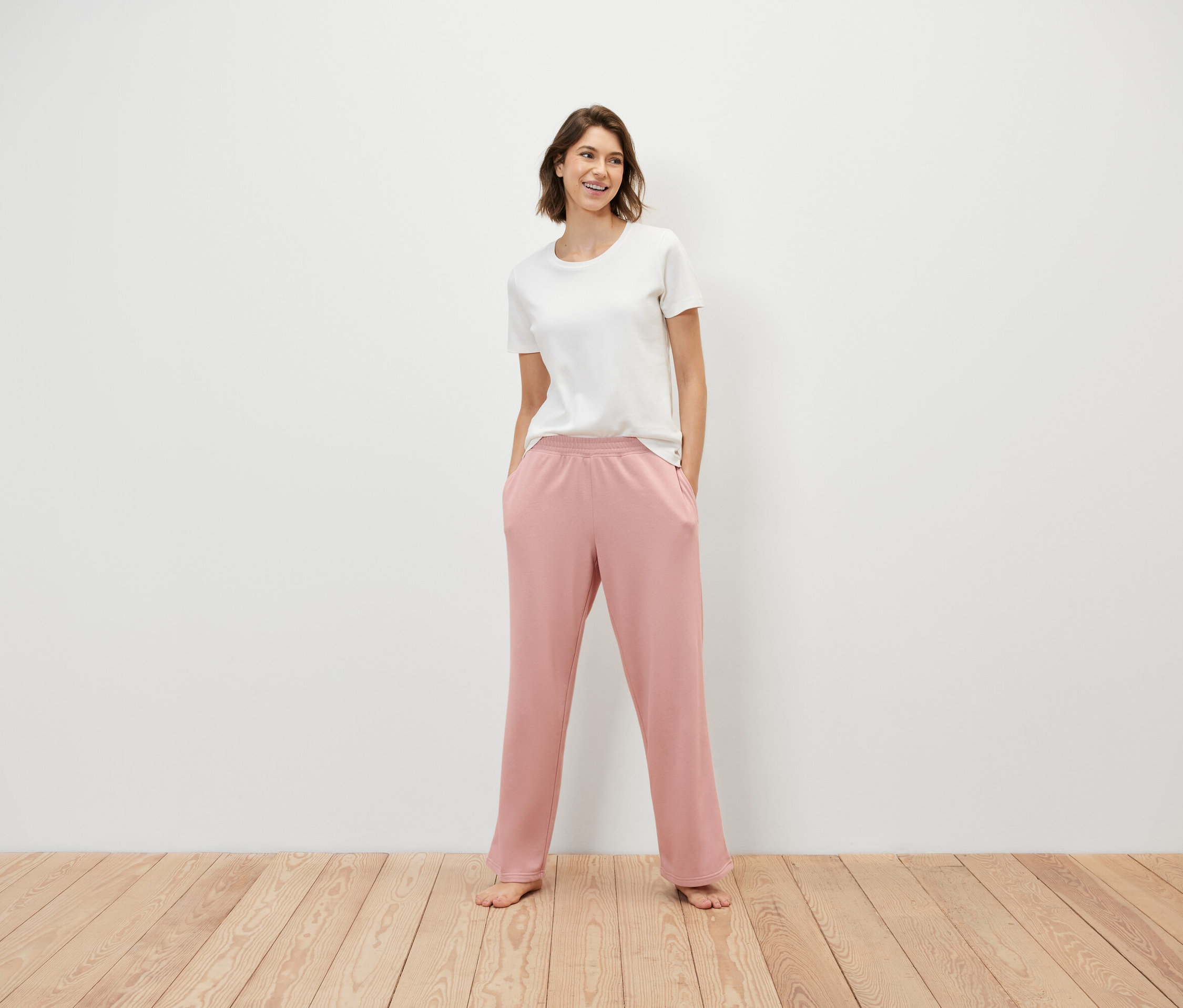 Une femme se tient debout, les mains dans les poches d'un pantalon de survêtement rose et portant un t-shirt blanc.