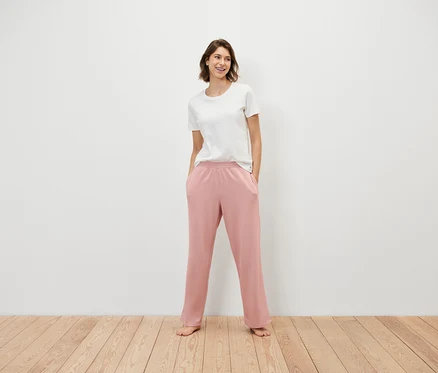 Une femme se tient debout, les mains dans les poches d'un pantalon de survêtement rose et portant un t-shirt blanc.