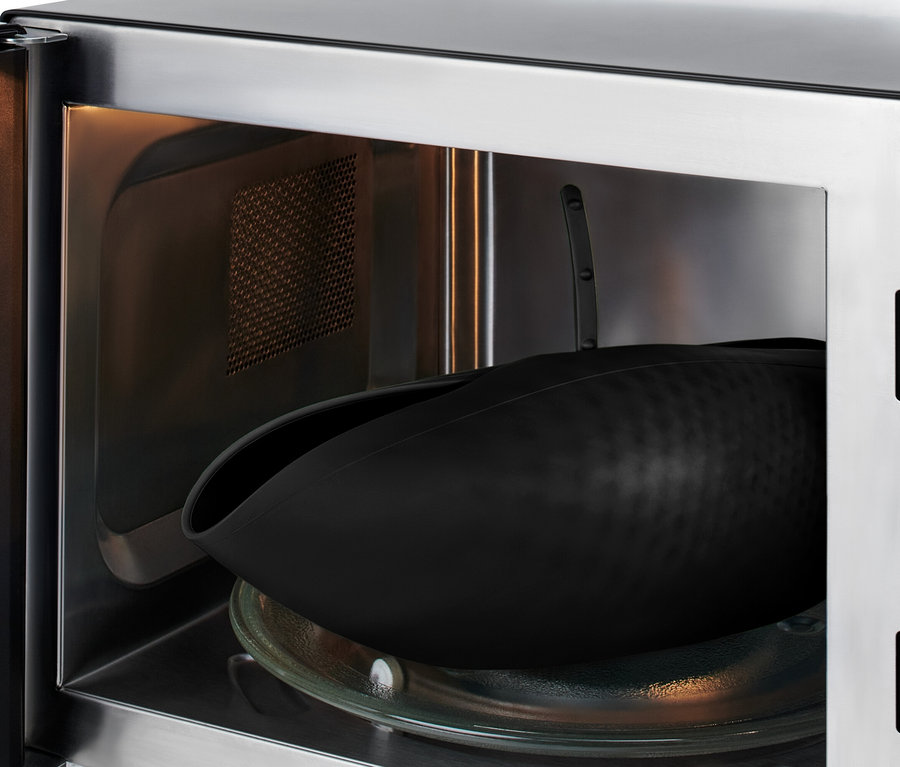 Un récipient noir en silicone repose sur un plateau en verre à l'intérieur d'un four à micro-ondes ouvert.