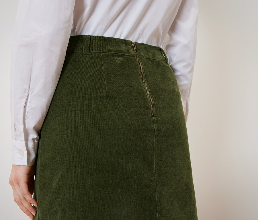Vue arrière d'une femme portant une jupe en velours côtelé vert olive et une chemise blanche.