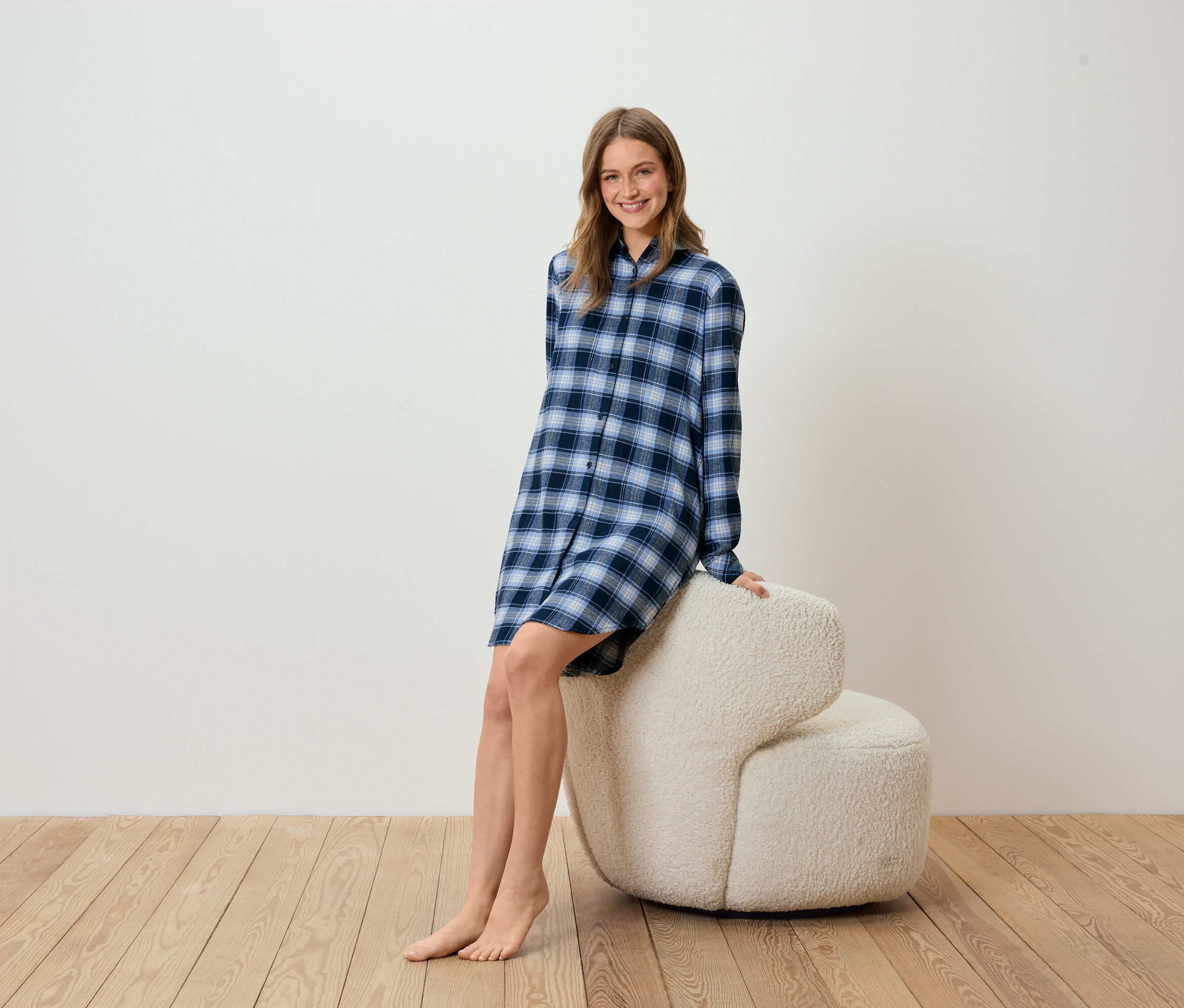 Femme assise sur un fauteuil beige portant une chemise de nuit à carreaux bleue.