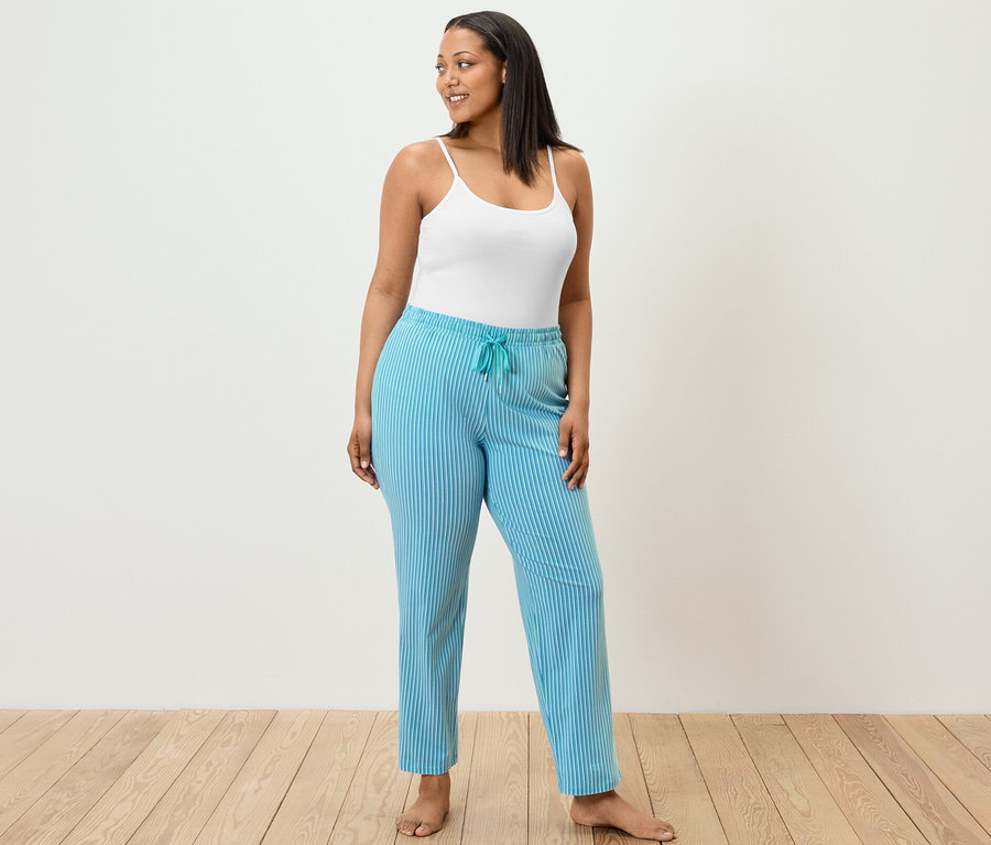 Une femme portant un pantalon de pyjama et 2 maillots de corps se tient debout.