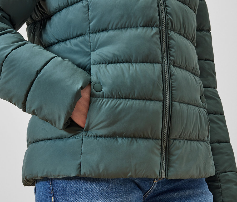 Main dans la poche d'une doudoune verte.