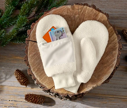 Mitaines couleur crème avec poche zippée sur un fond en bois avec des pommes de pin et des brindilles.