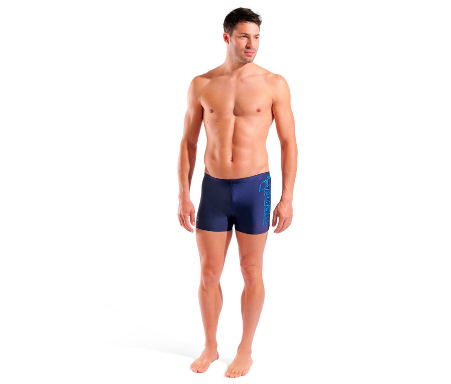 Un homme debout porte un maillot de bain arena Scratchy bleu marine.