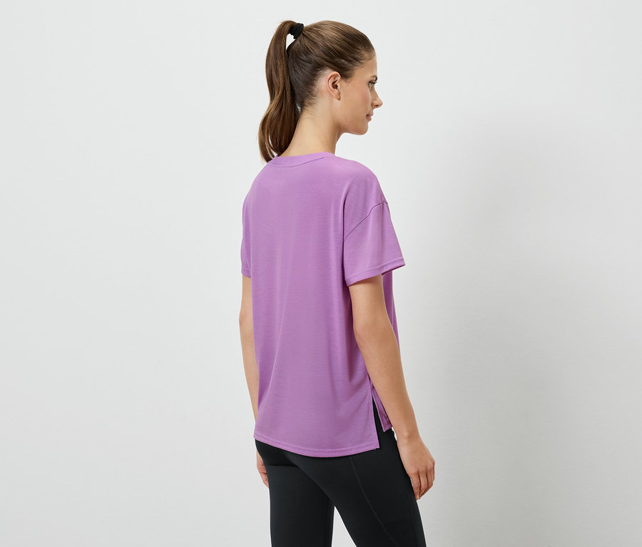 Femme portant un t-shirt lavande et des leggings noirs, debout, de dos.