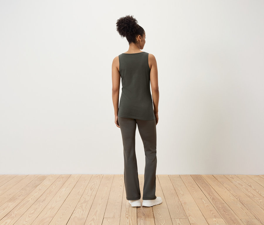 Une femme se tient dos à la caméra, vêtue d'un débardeur et d'un pantalon.