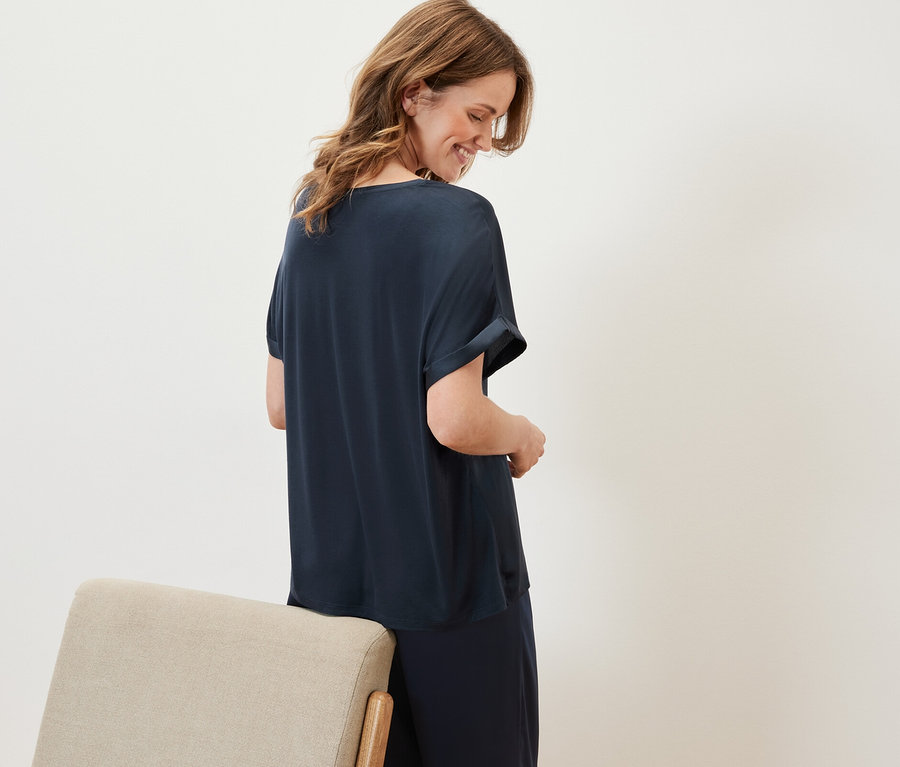 Une femme regarde vers le bas et porte une blouse bimatière bleu marine et un pantalon bleu marine.