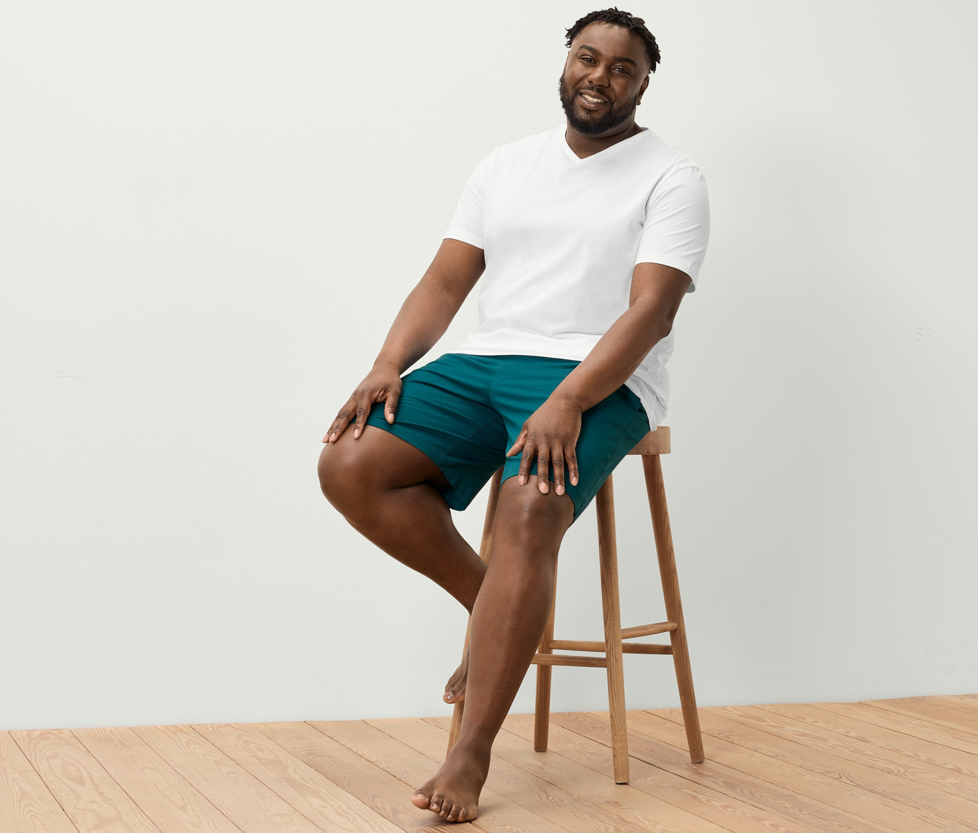 Un homme est assis sur un tabouret et porte un t-shirt blanc à encolure en V et un short relax.