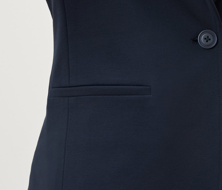 Détail d'un blazer bleu marine avec bouton et poche.