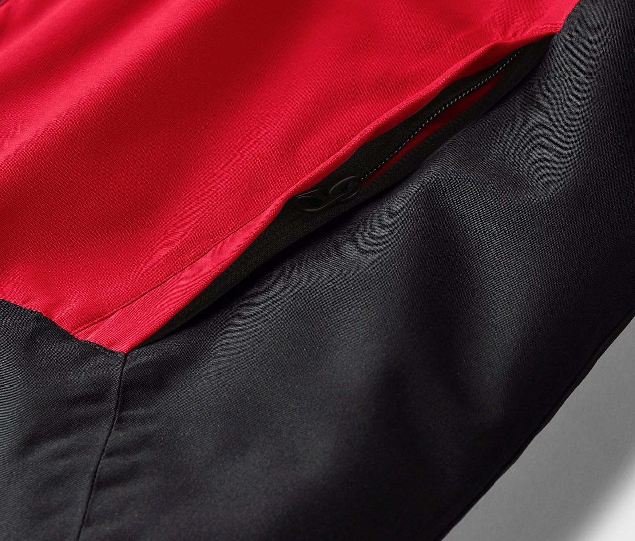 Détail d'une veste rouge et noire avec une poche zippée.