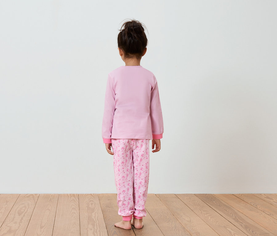 Une fille en pyjama rose, vue de dos.