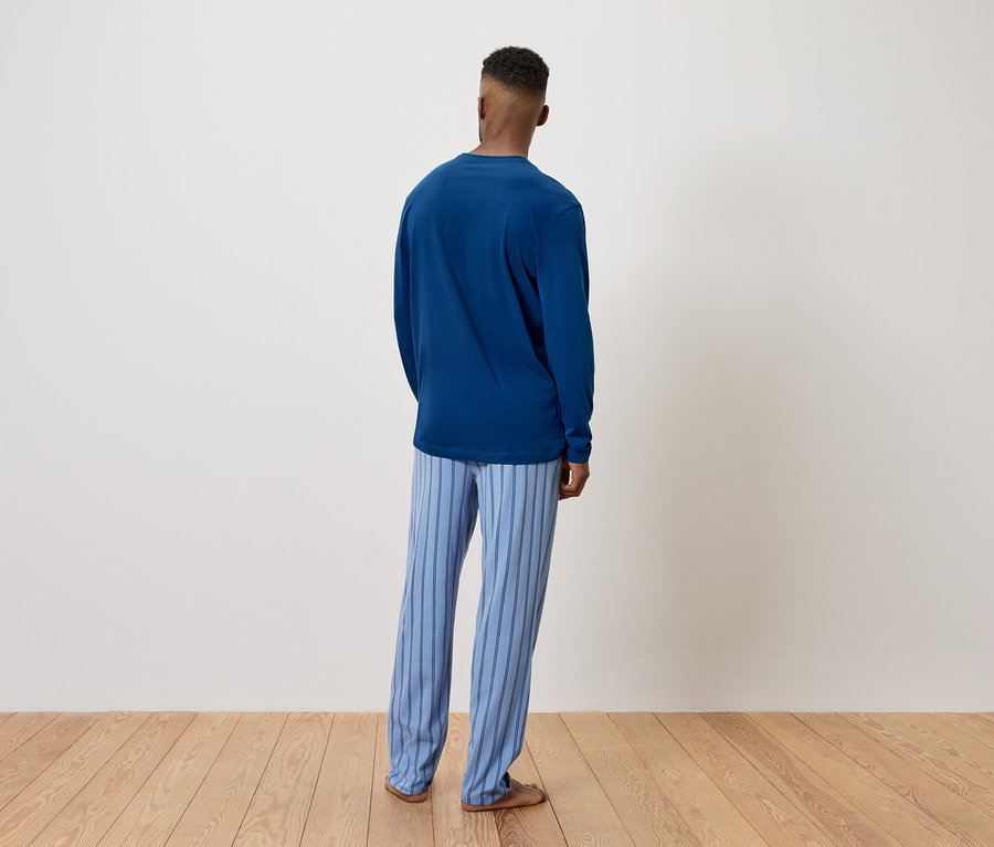 Un homme en pull bleu et pantalon rayé se tient dos à la caméra.