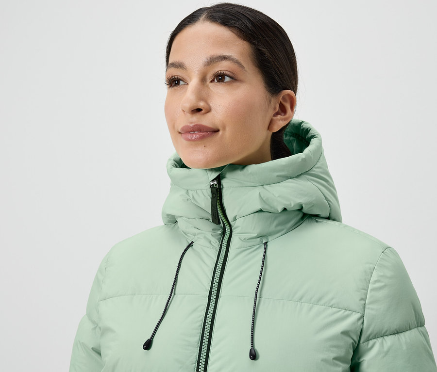 Une femme porte une doudoune vert clair.