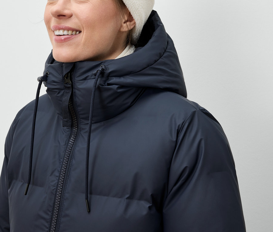 Une femme porte une doudoune bleu marine et un bonnet blanc.