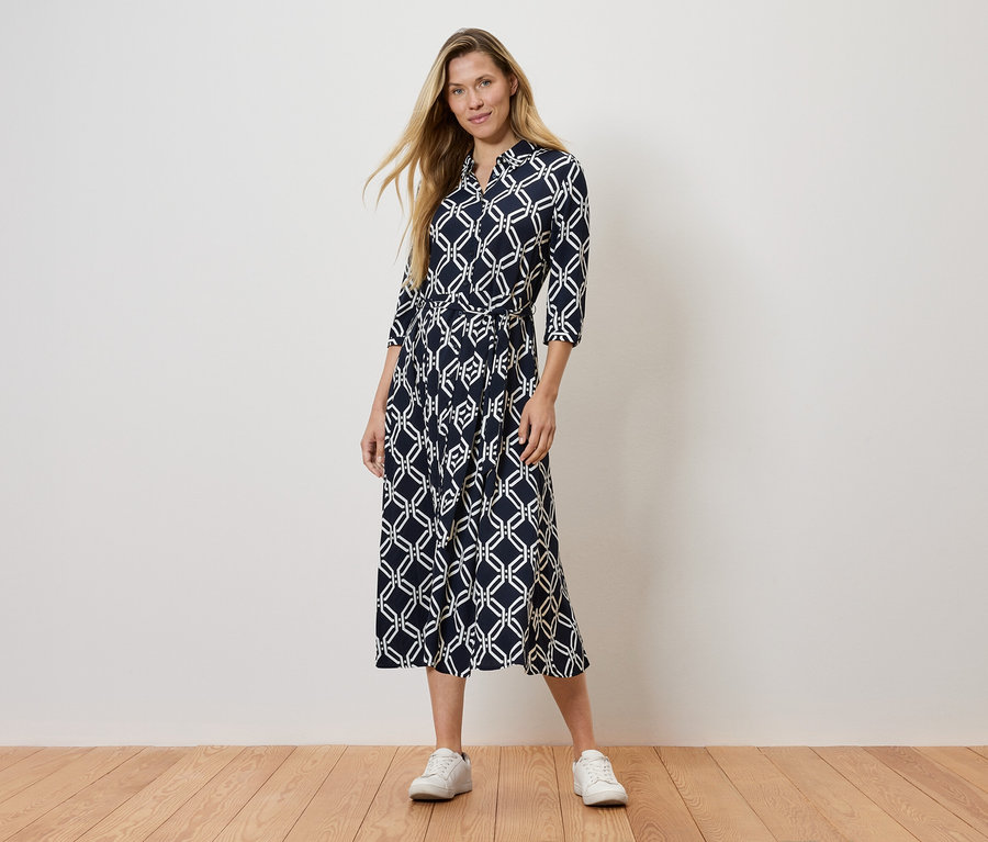 Une femme debout portant une robe bleu marine à motifs et des baskets blanches.