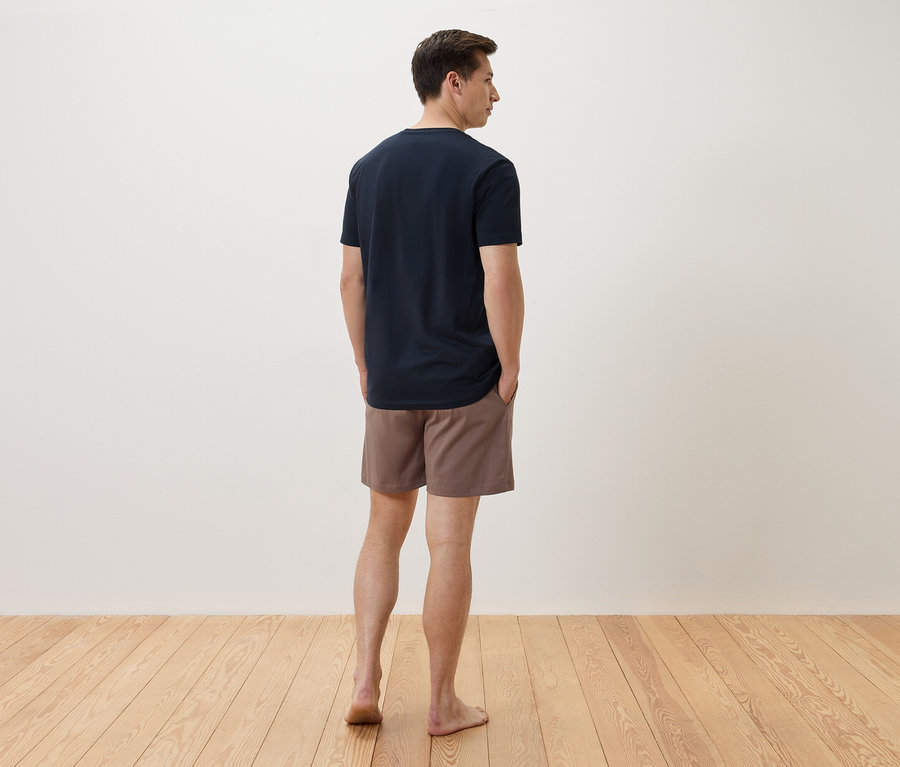 Un homme se tient dos à la caméra, portant un t-shirt bleu marine et un short marron.