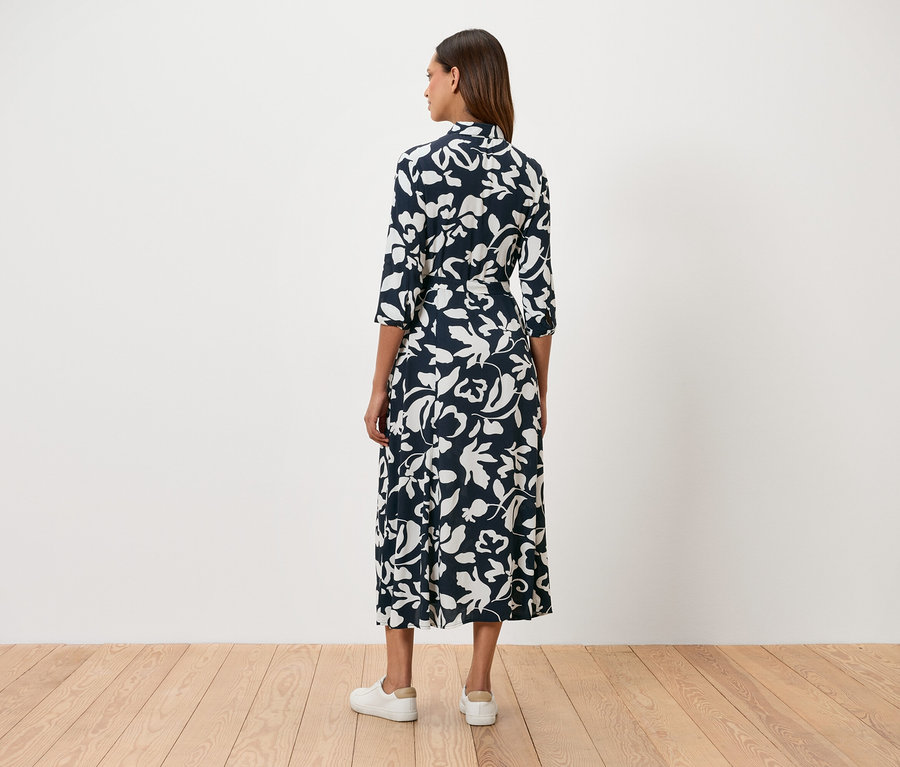 Une femme se tient dos à la caméra et porte une robe à fleurs bleu marine et des baskets blanches.