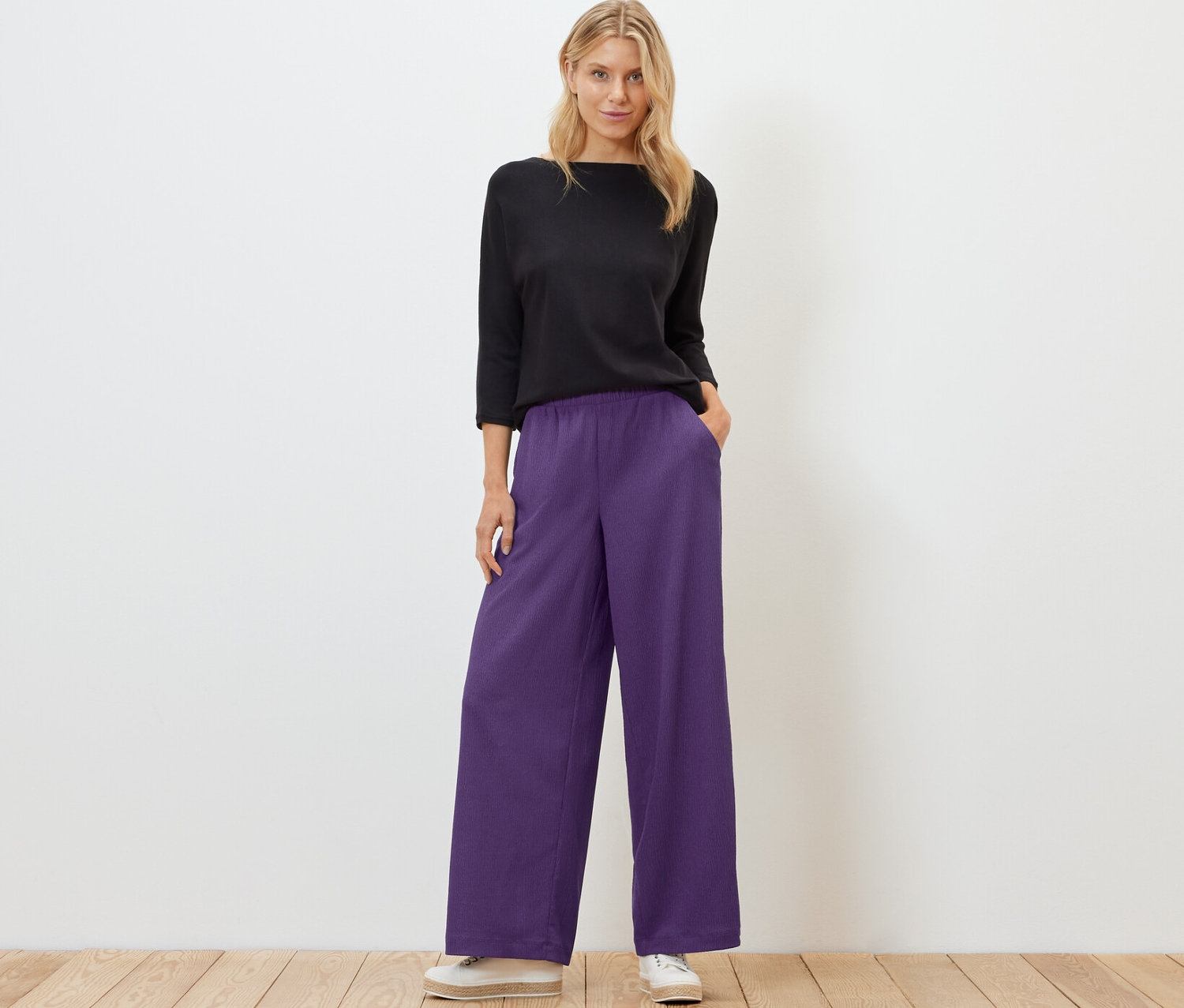 Femme posant dans un haut noir et un pantalon palazzo structuré violet.