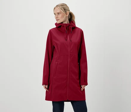 Blonde portant un manteau à capuche bordeaux zippé et un pantalon sur fond blanc.