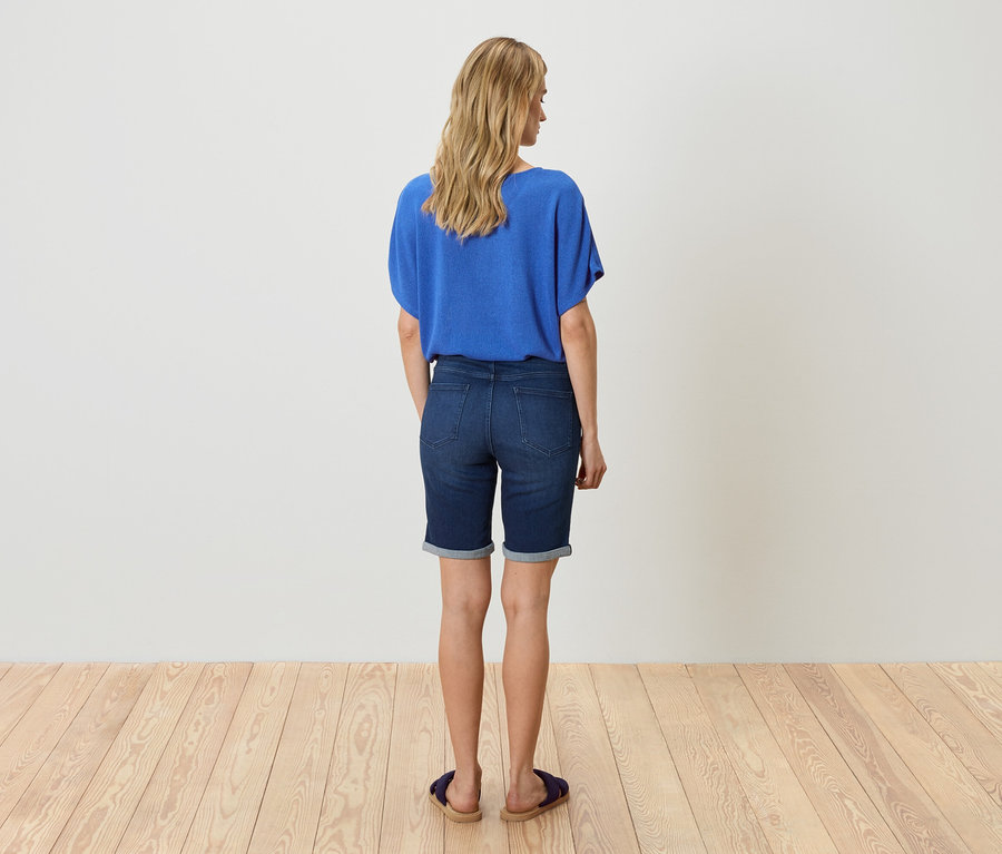 Femme de dos en chemisier bleu et short en jean.