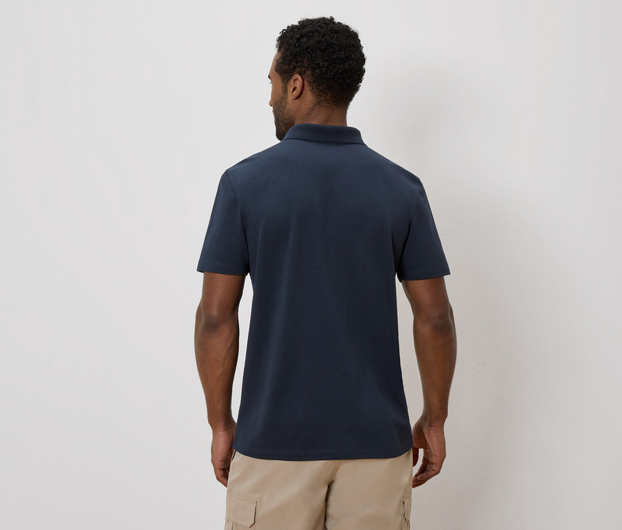 Vue arrière d'un homme aux cheveux foncés portant un polo bleu marine et un short cargo beige sur un fond uni.