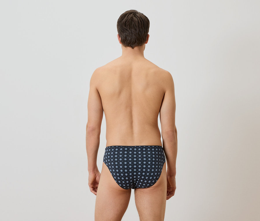 Un homme vu de dos portant un slip de bain bleu marine avec un motif floral blanc.