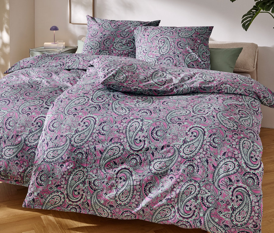 Gros plan d'un lit avec du linge de lit rose à motif cachemire.