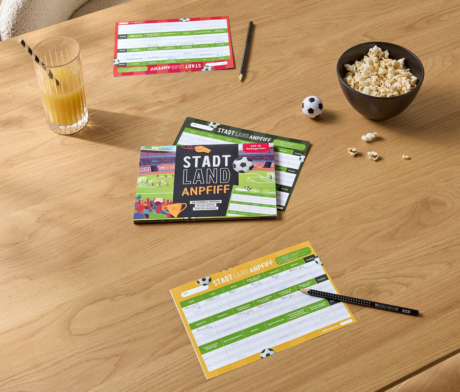 Sur une table en bois se trouvent des blocs de jeu, un verre de jus d'orange avec une paille, un bol de pop-corn et un petit ballon de football.