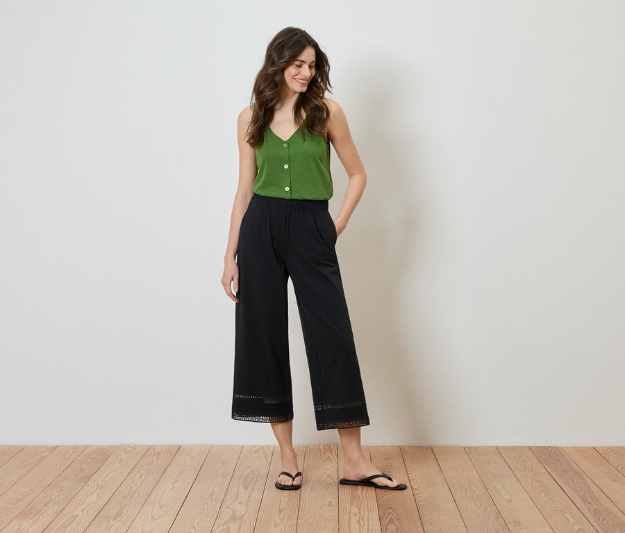 Une femme se tient debout, les mains dans les poches, portant un haut vert et une culotte noire avec des détails en dentelle à l'ourlet.