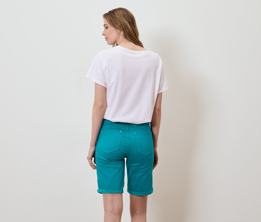 Une femme aux longs cheveux bruns se tient dos à la caméra, portant un t-shirt blanc et un short turquoise.