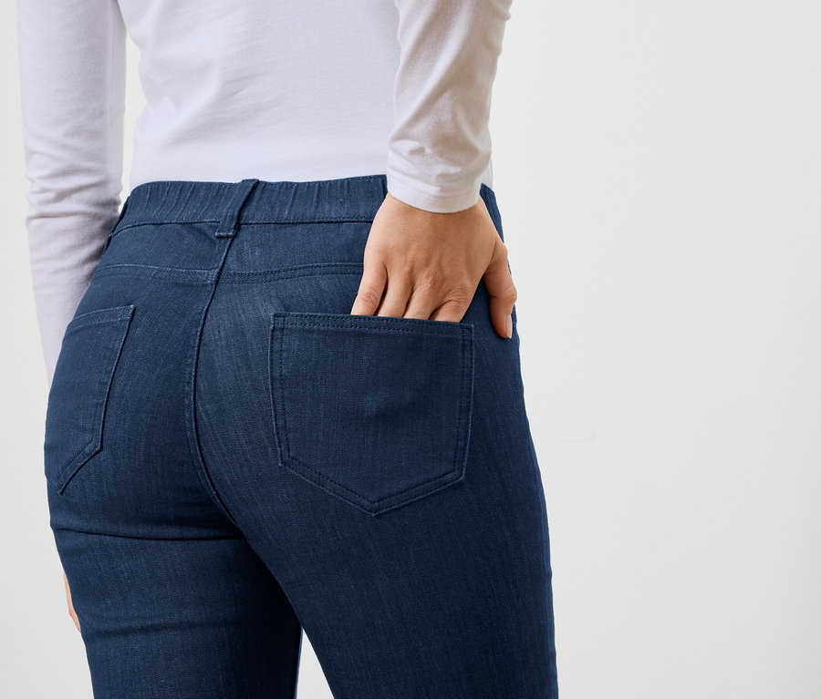 Femme, main dans la poche arrière d'un jean bleu marine, portant un haut blanc à manches longues.