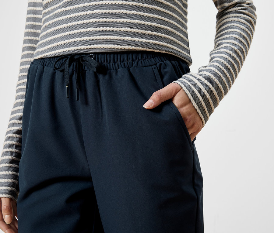 Femme portant un haut rayé et un pantalon bleu marine à cordon, la main dans la poche.