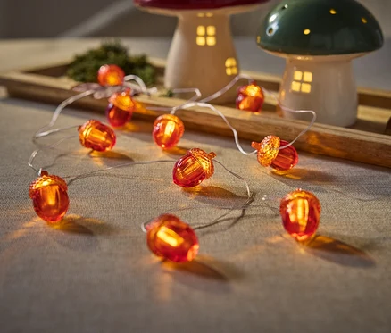Gros plan de guirlandes lumineuses en forme de glands sur une table à côté de lampes champignons sur un plateau en bois.