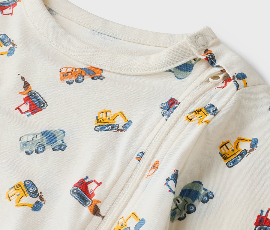 Gros plan d'une grenouillère crème pour bébé avec fermeture éclair et motif de camions de chantier.