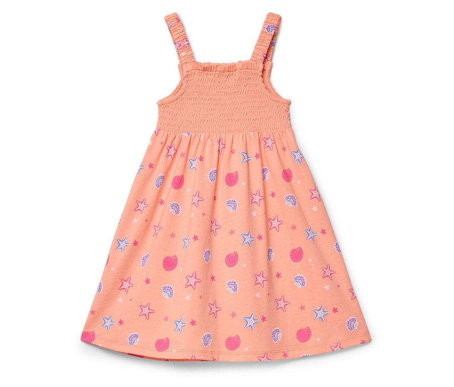 Une robe couleur pêche avec un motif de coquillages roses et d'étoiles de mer bleues posée sur un fond blanc.