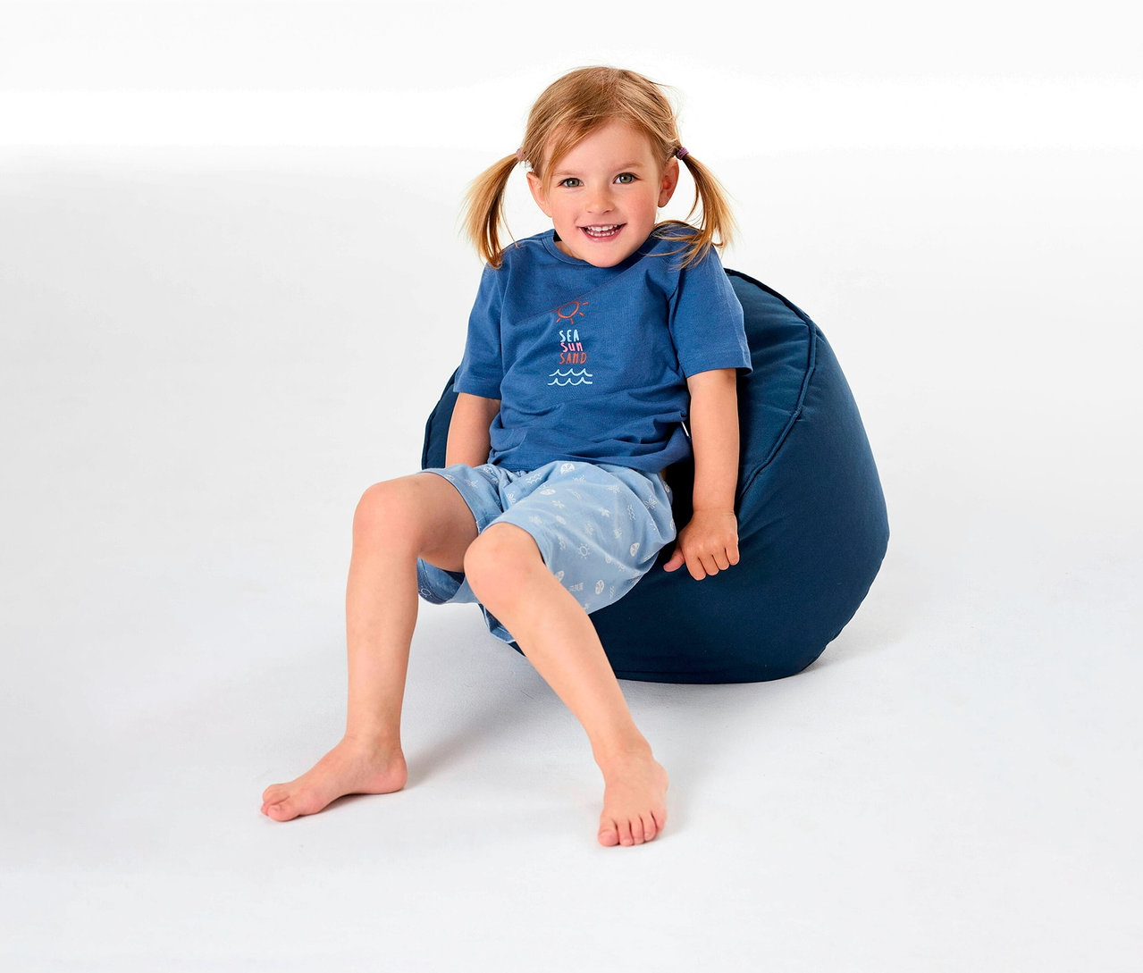 Une fille est assise sur un pouf et porte un pyjama court pour enfant SCHIESSER.